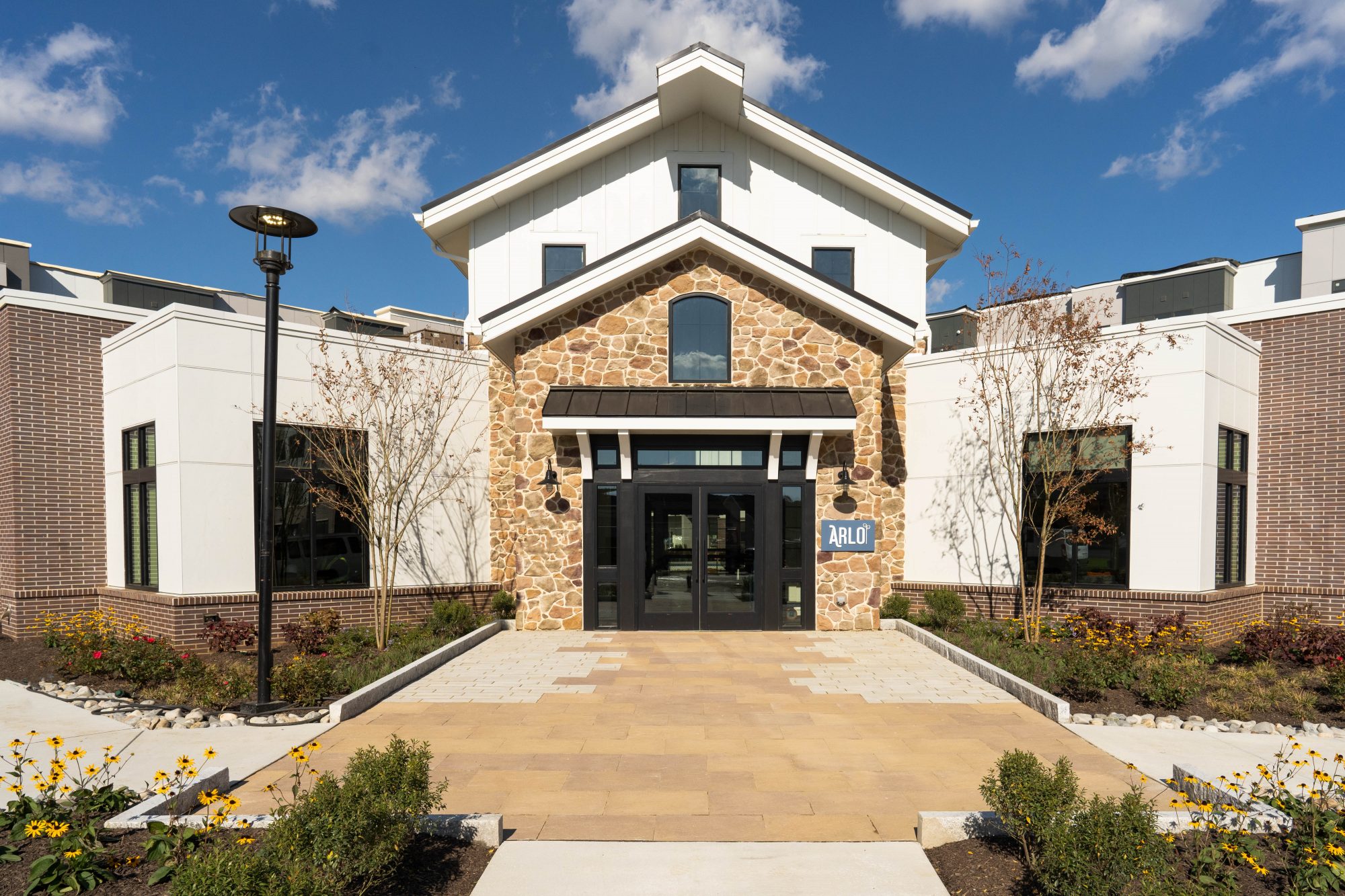 Willton A modern building with a stone and white facade, large windows, and a sign reading ARLO above the entrance. Brick and concrete paths lead to the door, surrounded by landscaped gardens and a lamppost.